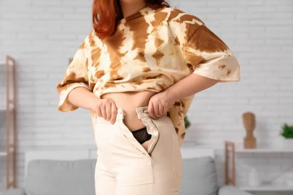 Image of woman trying to do her trousers up after pregnancy weight gain Almondsbury